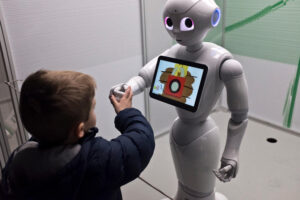 Photo of a boy touching the hand of a humanoid robot called Pepper, made by the Japanese company SoftBank.