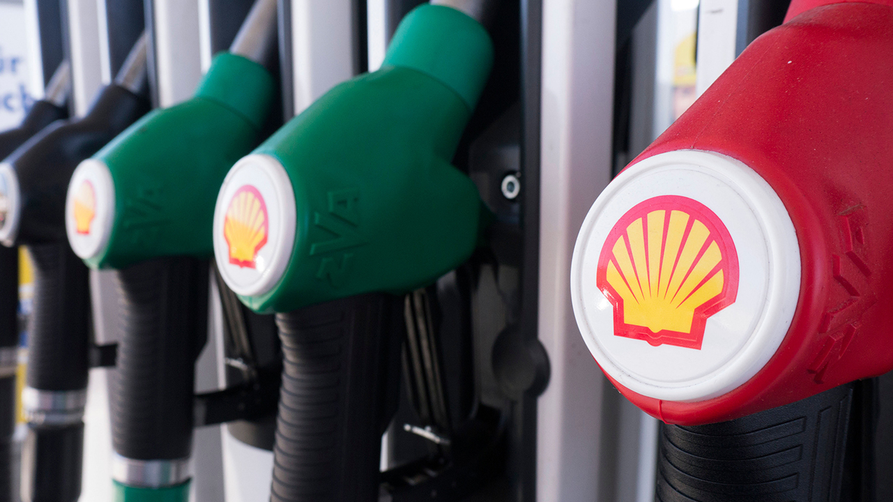 Four fuel pump nozzles at a Shell gas station, including three green and one red, each displaying the Shell logo.