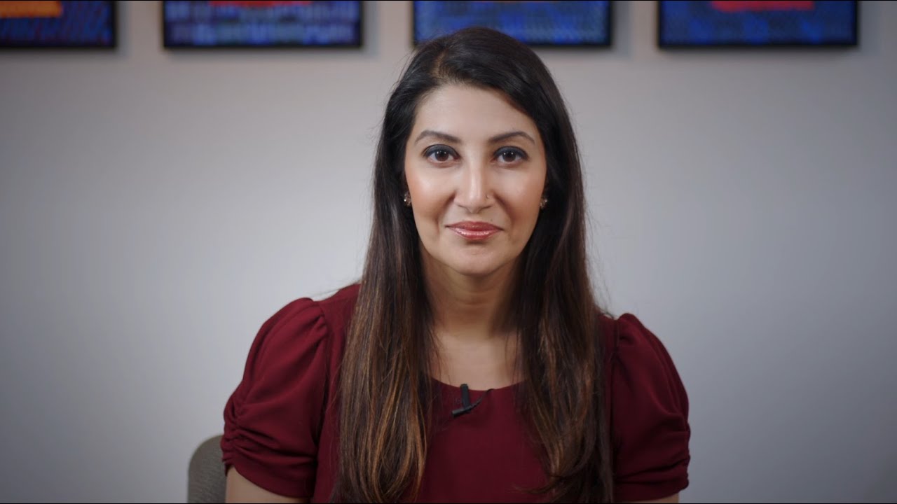Apurva Schwartz sits in front of a light-colored wall adorned with three framed artworks.